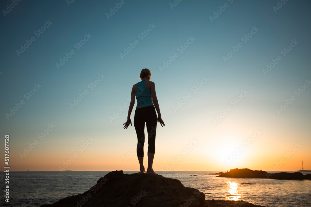 A woman practicing yoga on the ocean coast at pleasant sunset.