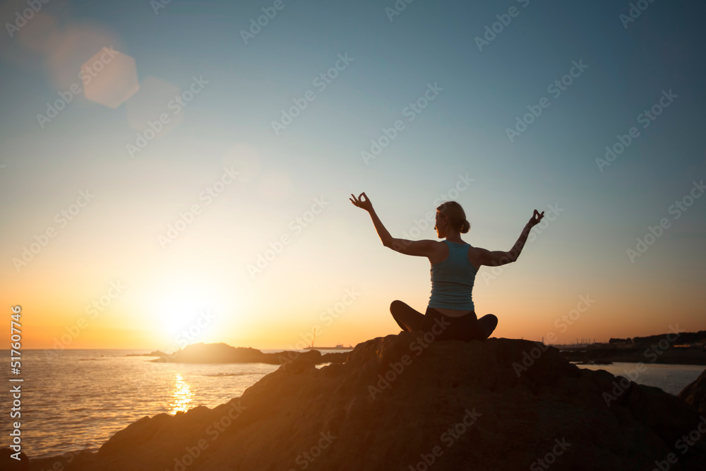 Silhouette of woman practicing yoga on the ocean coast at pleasant sunset.