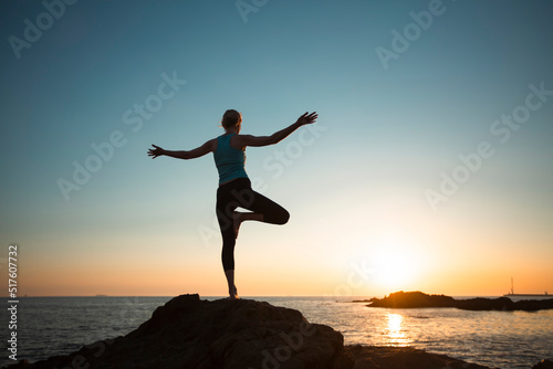 A female yogi exercises on a sea beach during a beautiful sunset.