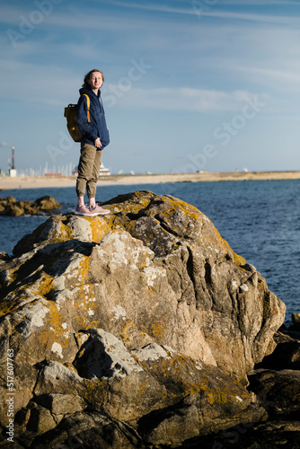 A woman tourist with a backpack stands on the sea coastal rocks.