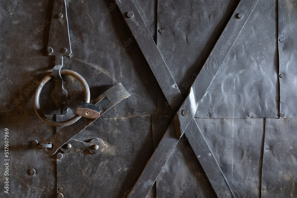 Naklejka premium Fragment of an old powerful black iron door. The metal surface is oxidized. There are brutal structural elements and a padlock. Background. Texture.