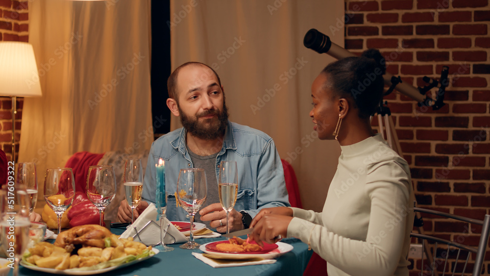 Positive man talking to relative while enjoying Christmas dinner at home. Festive happy family members gathered in living room to celebrate together traditional winter feast while eating and drinking.