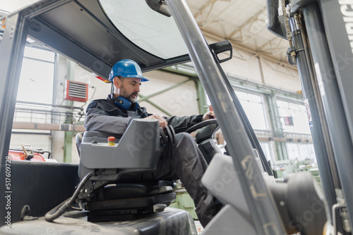 Happy mature man fork lift truck driver lifting pallet in storage warehouse .