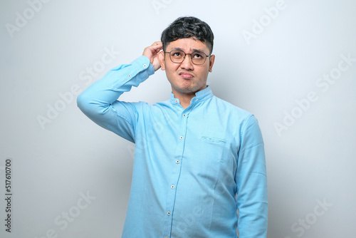 Handsome young Asian man wearing casual shirt and glasses standing with a shocked expression and holding his head © Reza