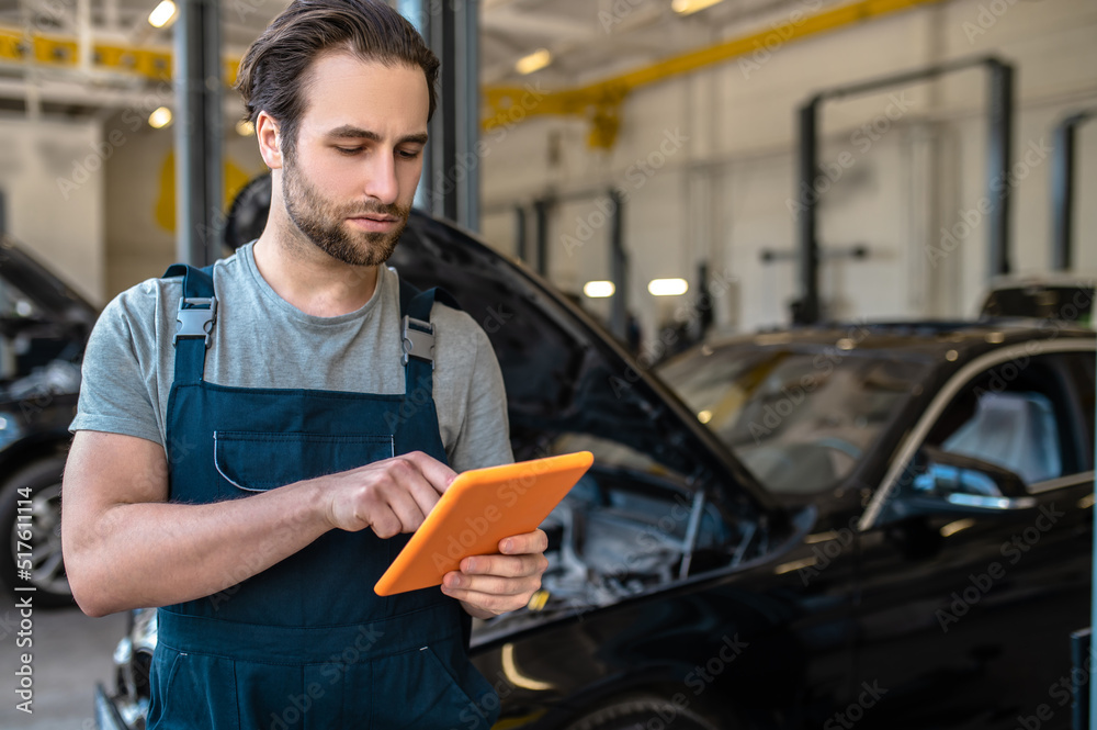 Auto mechanic looking at tablet standing in workshop Auto mechanic looking at tablet standing in workshop