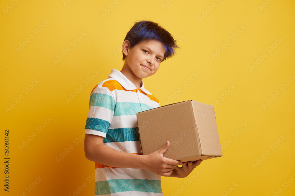 Teenage boy holding blank cardboard box over isolated yellow background, delivery concept Teenage boy holding blank cardboard box over isolated yellow background, delivery concept