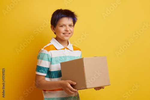 Teenage boy holding blank cardboard box over isolated yellow background, delivery concept