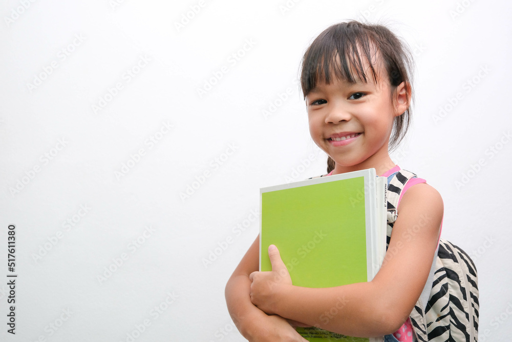 Back to school. Smiling little girl carrying a backpack holding books looking at the camera on a white background with copy space. Girl glad ready to study. Back to school. Smiling little girl carrying a backpack holding books looking at the camera on a white background with copy space. Girl glad ready to study.