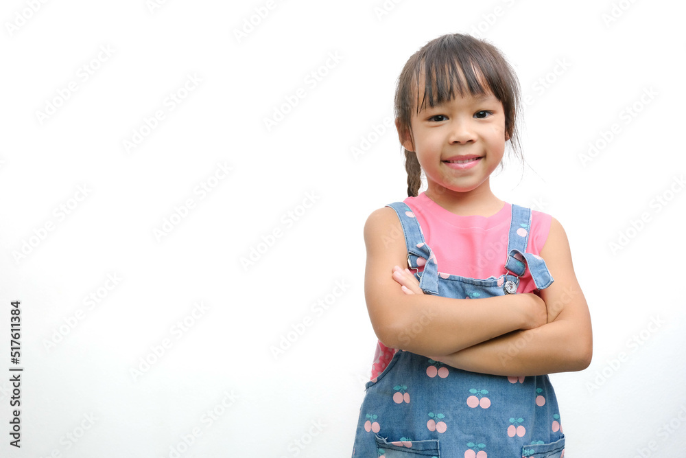 Asian cute little girl in jean overalls smiling showing her white teeth looking at the camera standing with her arms crossed on a white background with copy space. Asian cute little girl in jean overalls smiling showing her white teeth looking at the camera standing with her arms crossed on a white background with copy space.