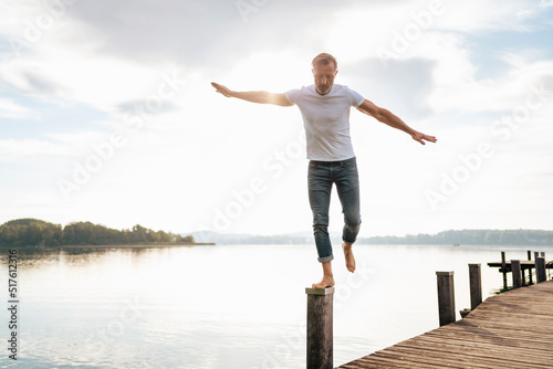 Mature man balancing on wooden post at pier by lake photo