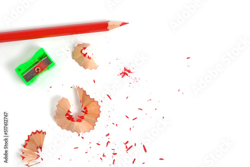 Sharpener and sharpened red pencil with sawdust on white background.