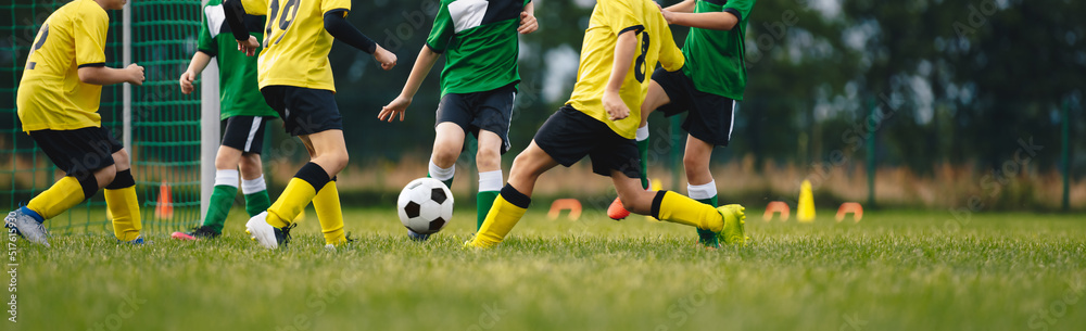 Kids play football on outdoor field. Children score a goal during a soccer game. Boys kicking ball. Running children in team jersey and cleats. School football club. Sports training for a young player Kids play football on outdoor field. Children score a goal during a soccer game. Boys kicking ball. Running children in team jersey and cleats. School football club. Sports training for a young player