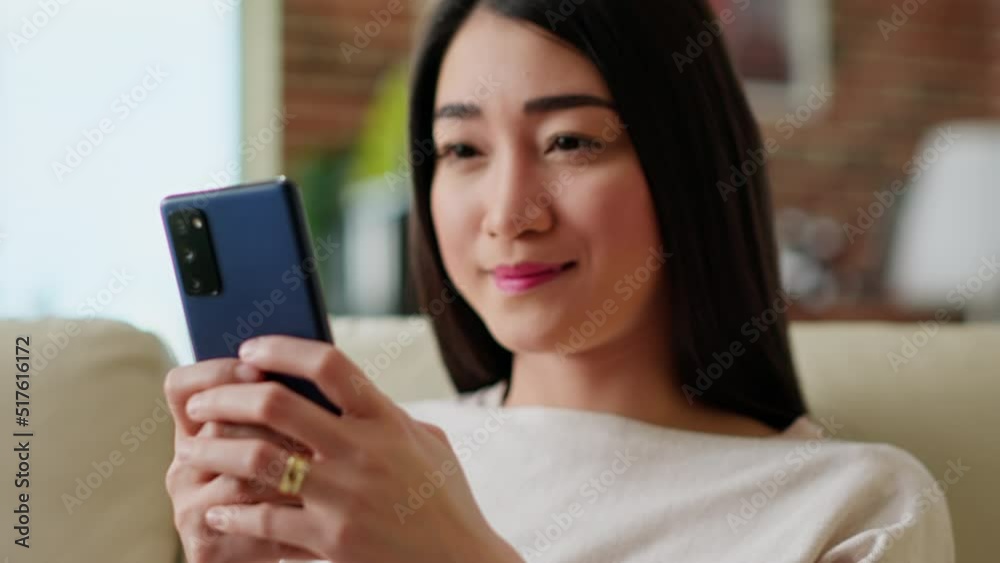 Cheerful young adult student chatting with colleague about next project assignment while sitting on sofa. Happy woman sending messages to friend using smartphone while smiling at camera. Handheld shot Cheerful young adult student chatting with colleague about next project assignment while sitting on sofa. Happy woman sending messages to friend using smartphone while smiling at camera. Handheld shot