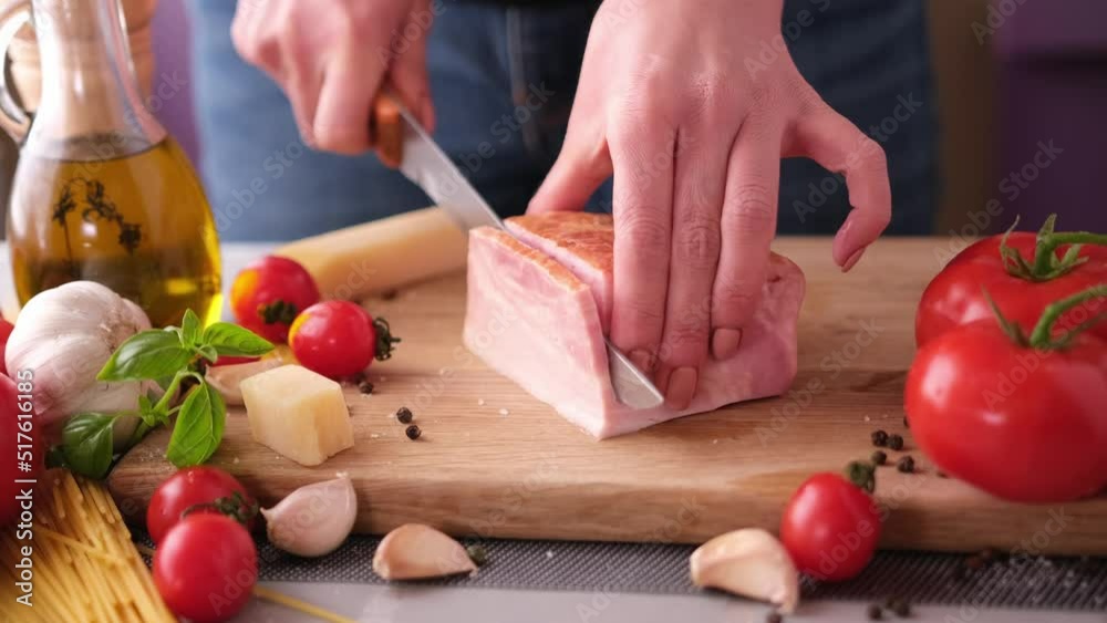 Making pasta carbonara - Slicing traditional pancetta bacon into pieces on a wooden cutting board with a knife