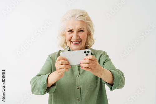 Grey senior woman smiling while playing online game on mobile phone