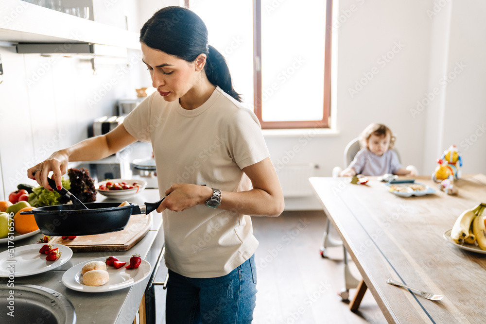 Smiling young mother cooking breakfast in the kitchen Smiling young mother cooking breakfast in the kitchen