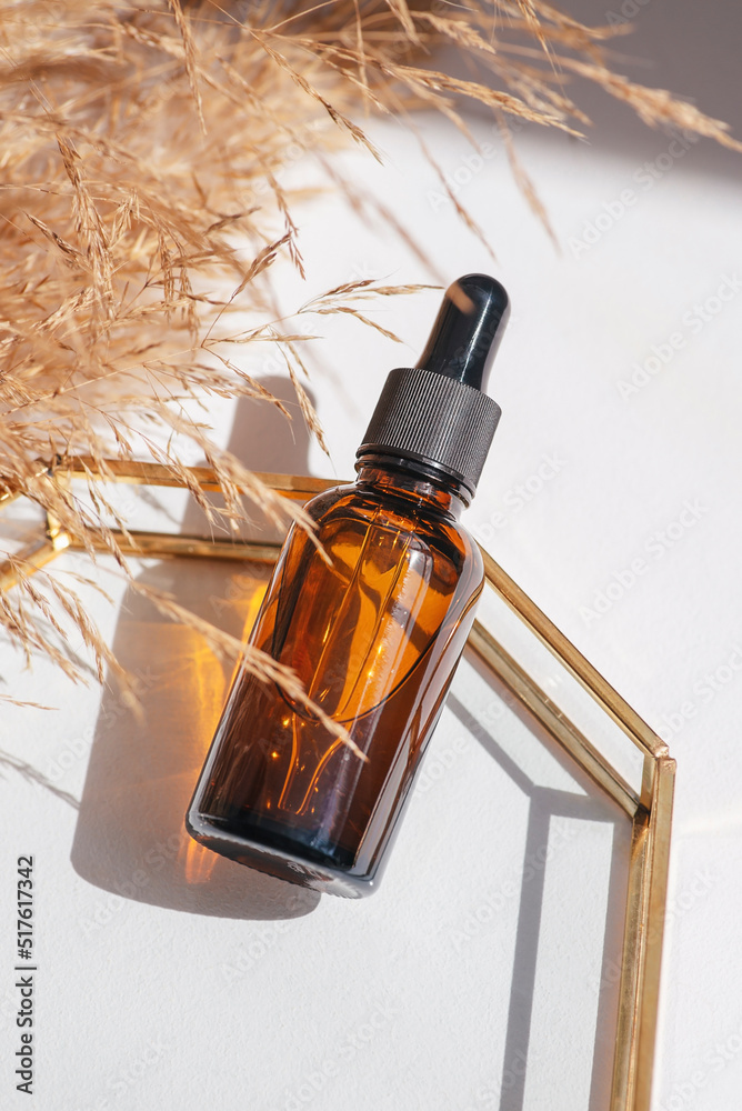 Amber glass bottle dropper pipette with serum or essential oil on glass plate for product presentation. Skincare cosmetic and with wildflowers. Beauty concept for face body care Amber glass bottle dropper pipette with serum or essential oil on glass plate for product presentation. Skincare cosmetic and with wildflowers. Beauty concept for face body care
