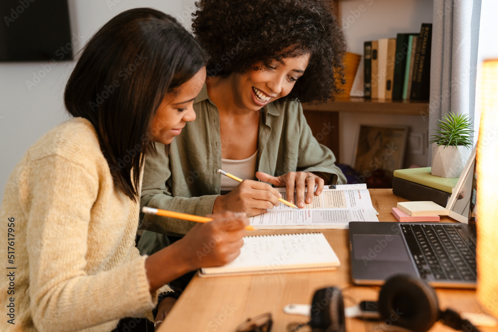 Black girl writing in exercise book while doing homework with her mother Black girl writing in exercise book while doing homework with her mother