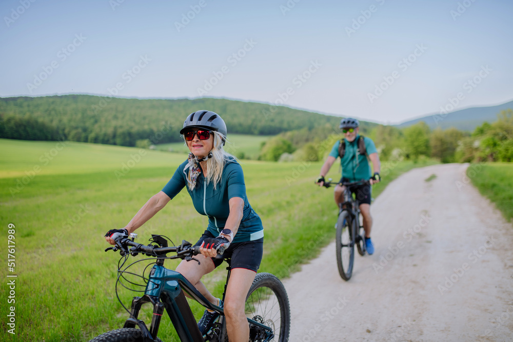 Active senior couple riding electric bicycles on trail at summer park, healthy lifestyle concept.