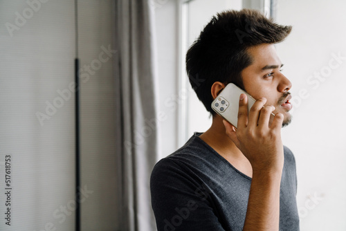 Young handsome indian man talking on phone in sunny room