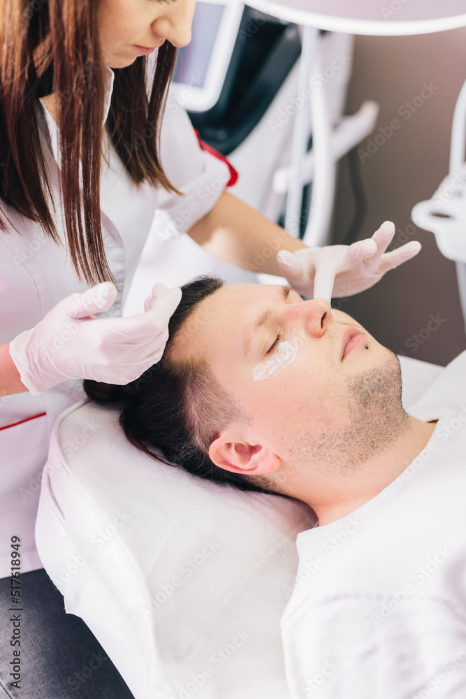 Cosmetologist applying anesthetic cream on man face in beauty salon Cosmetologist applying anesthetic cream on man face in beauty salon
