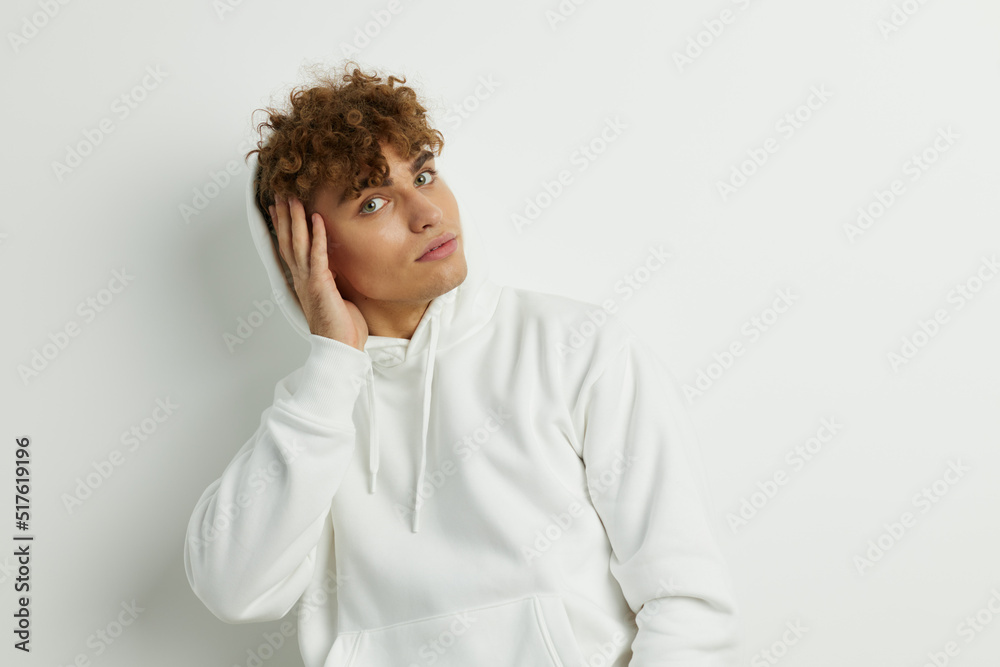 a cute man stands on a white background in a white hoodie on his head and holds his hand near his face a cute man stands on a white background in a white hoodie on his head and holds his hand near his face