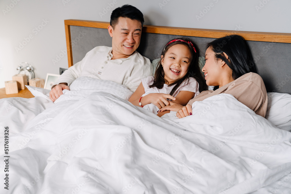 Obraz premium Happy asian family with little girl lying in bed together at home