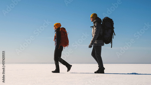 The couple of tourists with backpacks traveling through the snow field