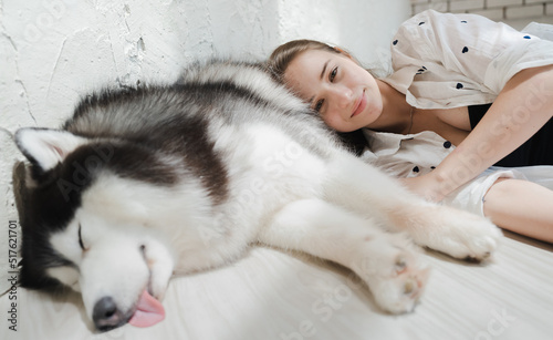 Sleeping alaskan malamute big dog and young woman lying on floor. Beautiful girl love pet. Portrait of female owner and adorable malamute happy close friend, together have fun at home in bedchamber. © Nassorn