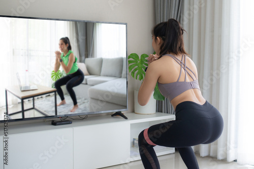 Young woman doing online weight training with a personal trainer in the living room at home. She exercises to stay healthy.