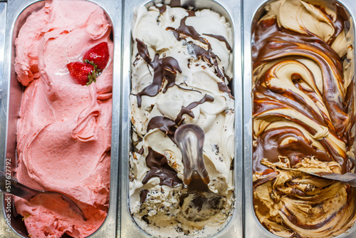 Tre vaschette di gelato artigianale al gusto fragola, stracciatella e tiramisù nella vetrina di una gelateria artigianale pronte per essere vendute photo
