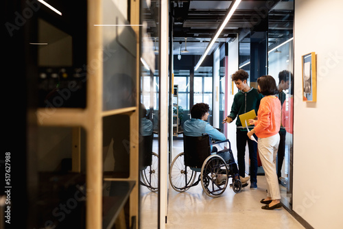 Multiracial colleagues discussing with businessman sitting in wheelchair at office corridor