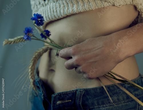 young Woman holding a bunch of summer flowers in front of stomach, cropped upper body, 