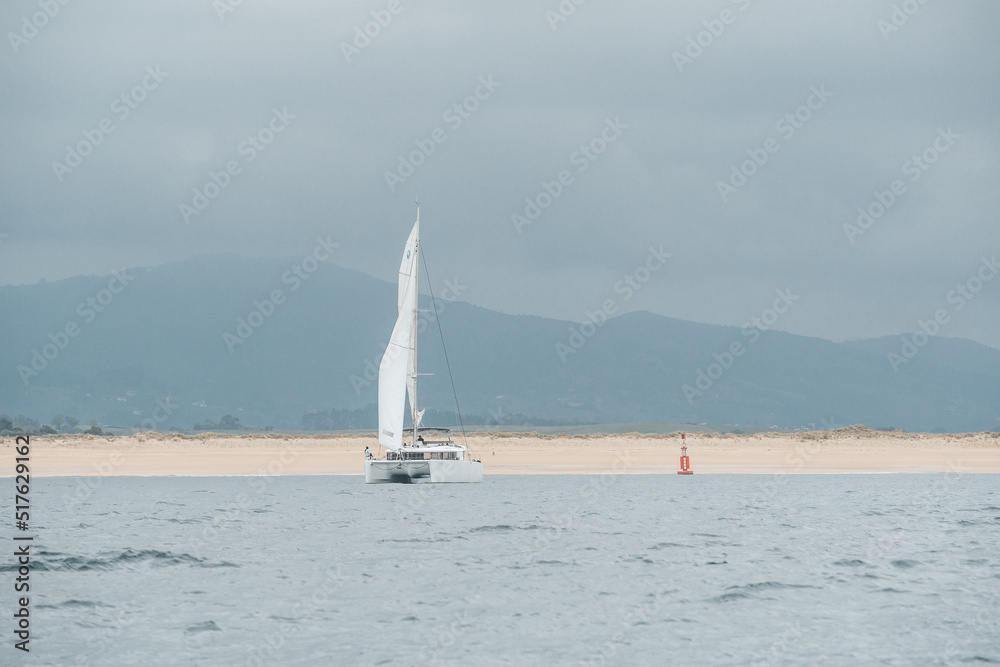 Catamarán navegando en un día nublado frente a hermosa playa desierta