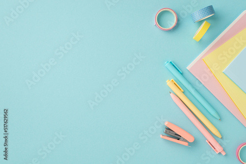 School accessories concept. Top view photo of school supplies mini stapler adhesive tape colorful pens and copybooks on isolated pastel blue background with copyspace