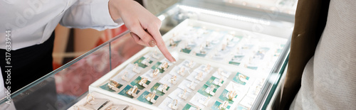 Картината върху платно Cropped view of seller pointing at jewelry rings in glass showcase near customer in shop, banner