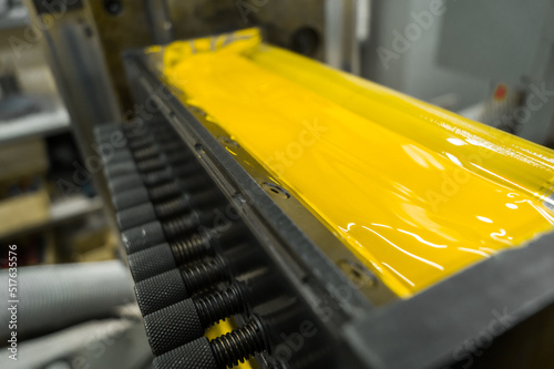 Yellow ink in the paint system compartment of a modern flexographic printing press in a print shop. Yellow paint in the ink feeder on the printing cylinder. Selective focus