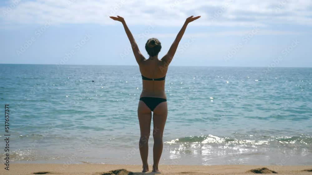 Young girl in bikini standing on sea beach and enjoying view. Beautiful woman relaxing on ocean shore during summer vacation travel. Concept of rest at the resort coastline. Slow motion Close up Young girl in bikini standing on sea beach and enjoying view. Beautiful woman relaxing on ocean shore during summer vacation travel. Concept of rest at the resort coastline. Slow motion Close up