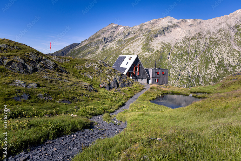 View of the Scaletta hut near the Greina Pass in Blenio, Switzerland. In the foreground is the path leading to the hut. In the background are the high mountains overlooking the scene.