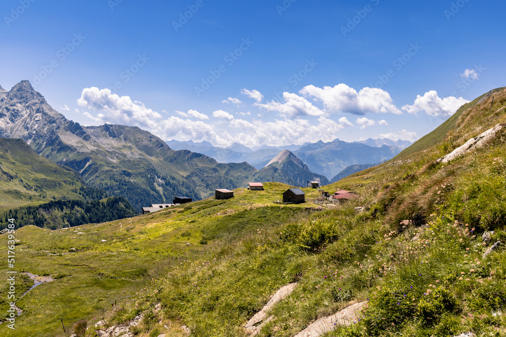 Aerial view of a very large and majestic alpine landscape in the Lord of the Rings style. In the midground is a small alpine village composed mainly of alpine pastures. Some high mountains in the