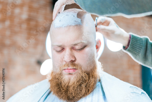 Εκτύπωση καμβά A bearded man is being shaved his head in barber salon.