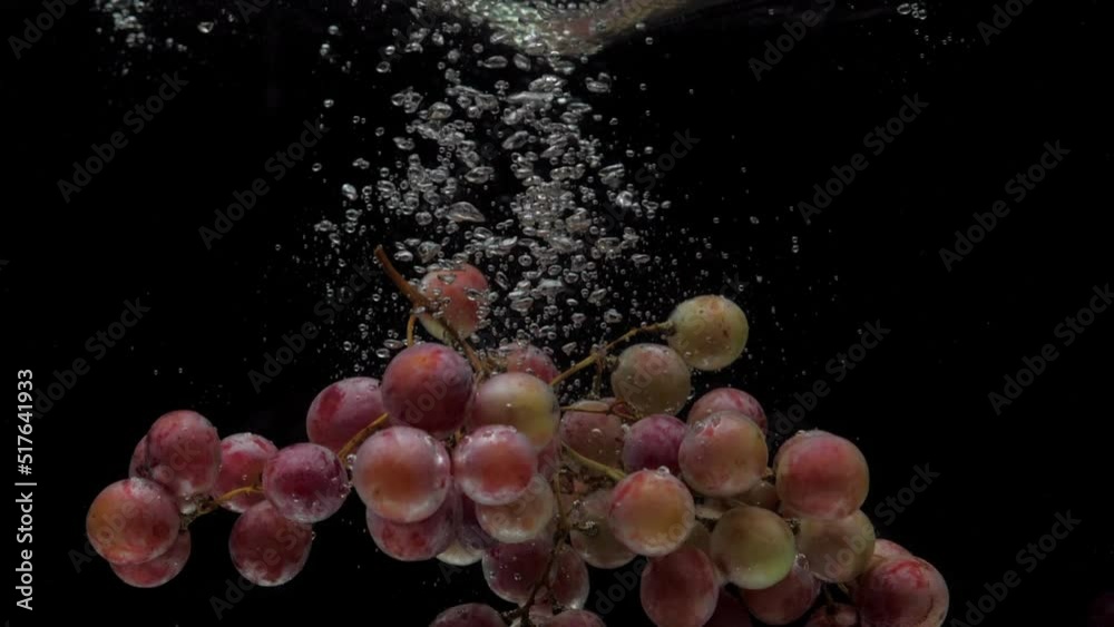 Slow motion red grapes falling into transparent water on black background. Fresh fruit splashing in aquarium. Healthy food, diet, air bubbles Slow motion red grapes falling into transparent water on black background. Fresh fruit splashing in aquarium. Healthy food, diet, air bubbles