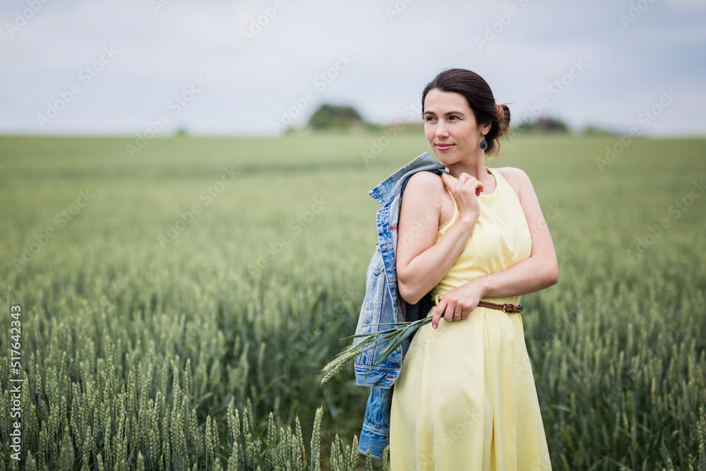 Lifestyle portrait of young stylish woman walking by wheat field and holding ears in his hands, wearing yellow dress Lifestyle portrait of young stylish woman walking by wheat field and holding ears in his hands, wearing yellow dress