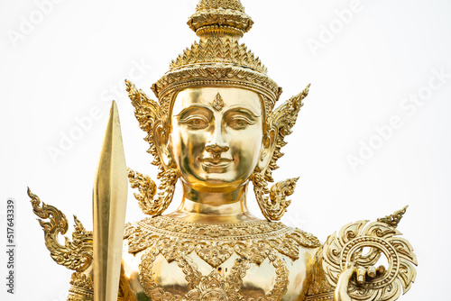 A golden graven image standing with a sword and rowel in his hand. Jada's multiple layers are placed on his head. He was standing on golden bases against a white backdrop photo