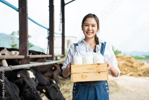 Portrait of Asian woman dairy farmer holding bottle of milk in cowshed © Kawee