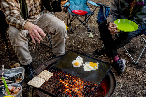 Breakfast camp cooking. Man cooking grilling eggs and warming bread on a cast iron plate over the camp fire. Camping lifestyle