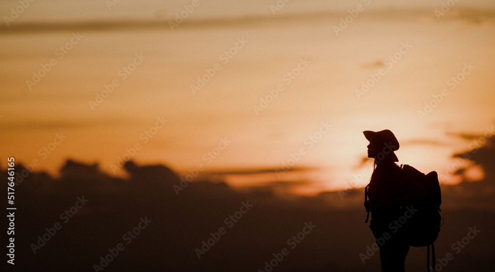 Naklejka premium Young woman with backpack hikes in the mountain with a beautiful view through the sunset with warm red light. Blurred silhouette background.