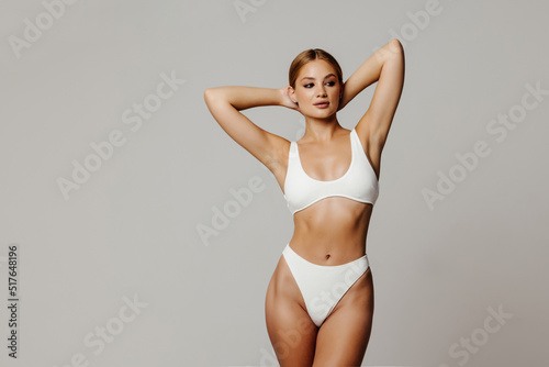 Perfect forms. Attractive young woman in white tank top and panties posing while standing against white background