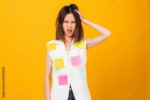 Boring young Asian woman hand touching on head and a sticky note on the clothes, stand on studio shot yellow background.