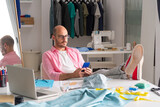 male clothing designer, sitting on a chair, typing on his smartphone, resting from work in his pattern making workshop
